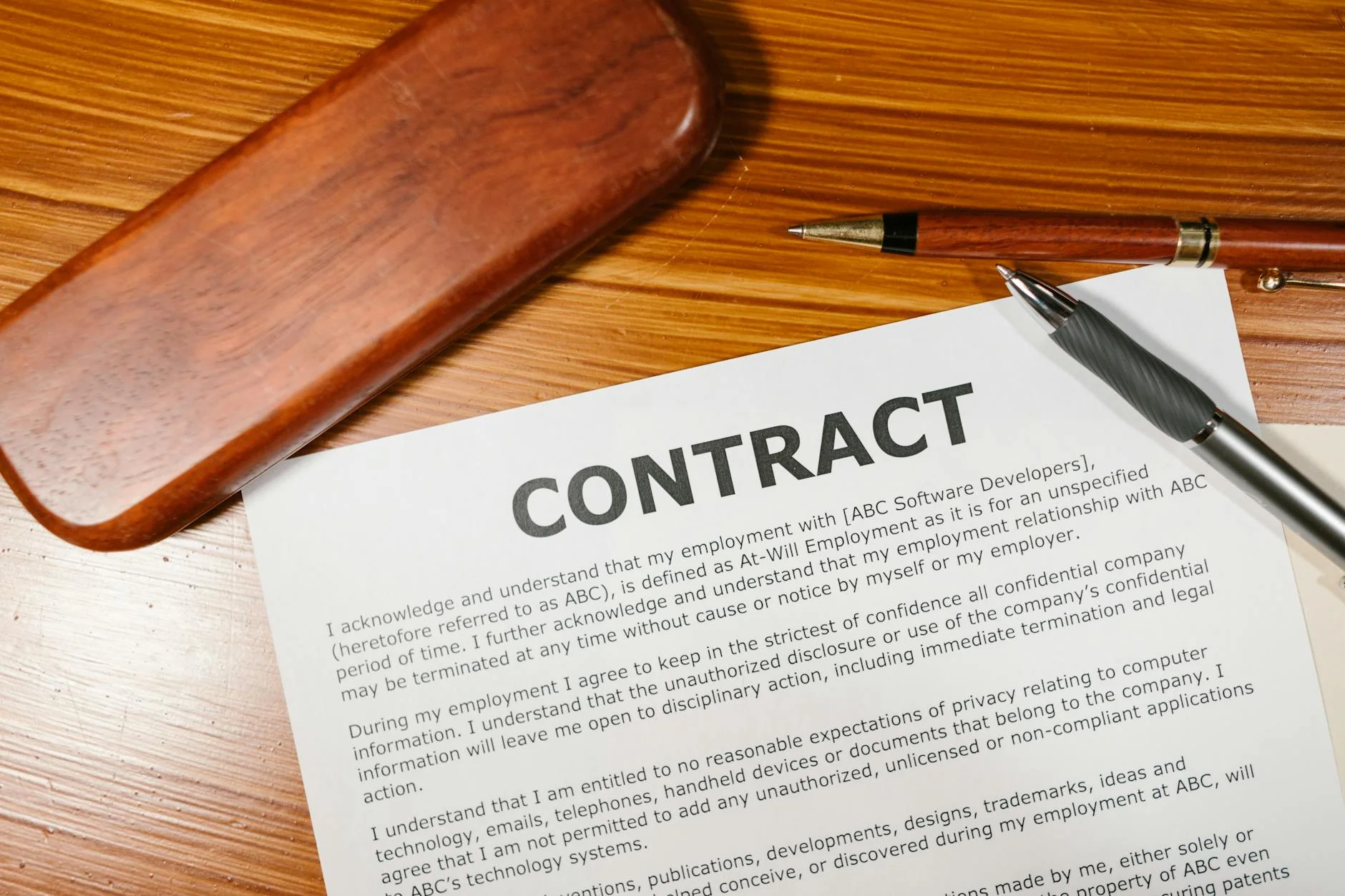 Two business people signing a printed contract across a wooden desk