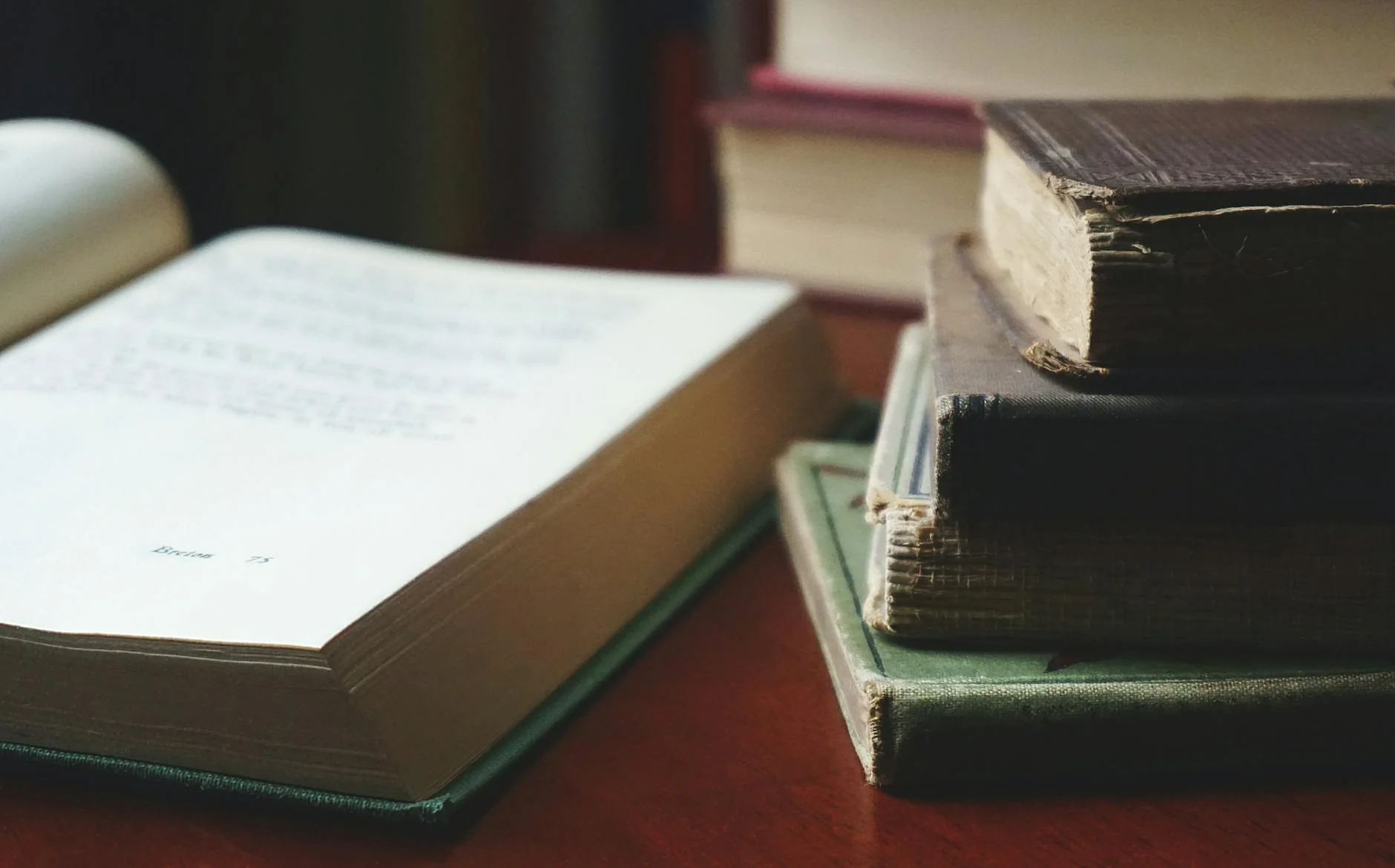 Stack of hardcover and paperback books on a wooden table next to a children's picture book