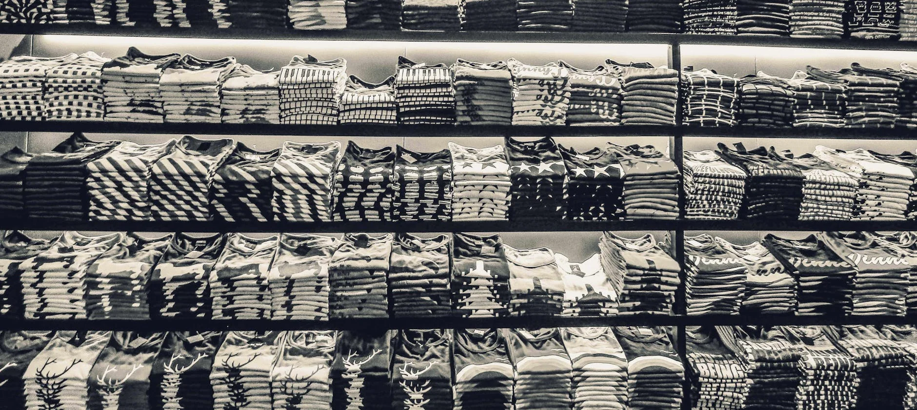Rows of folded knit garments and hanging shirts on a retail clothing rack