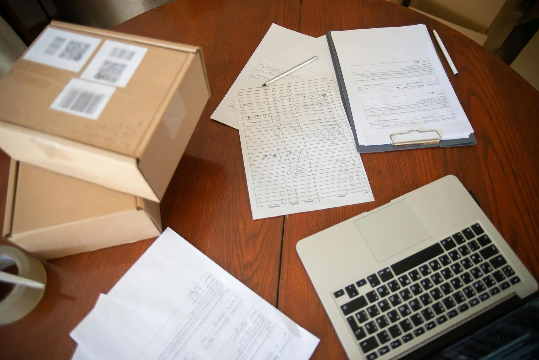 A printed list of requirements ticked off on a wooden desk beside shipping boxes