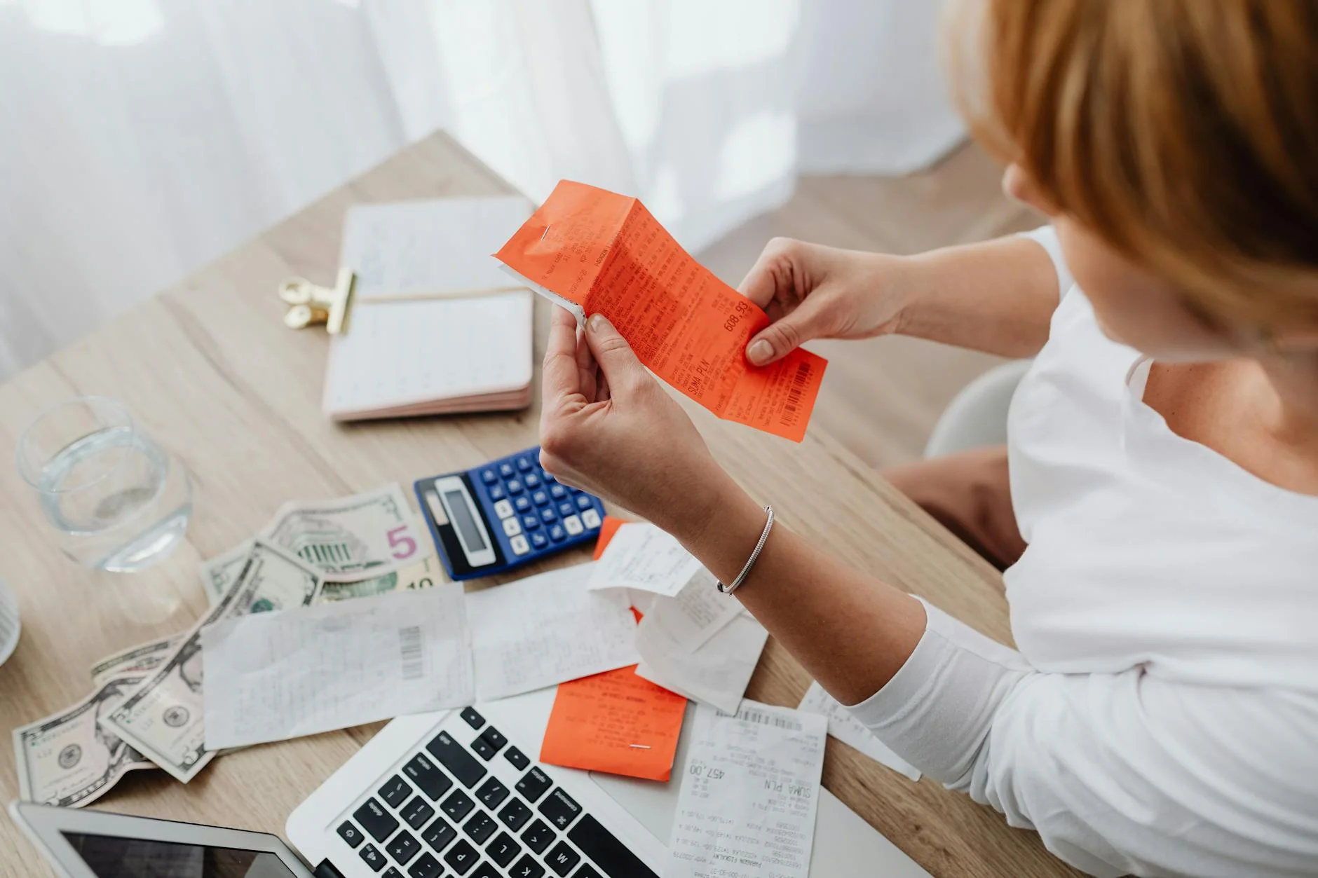 A person at a desk reviewing printed invoices and a calculator next to a laptop