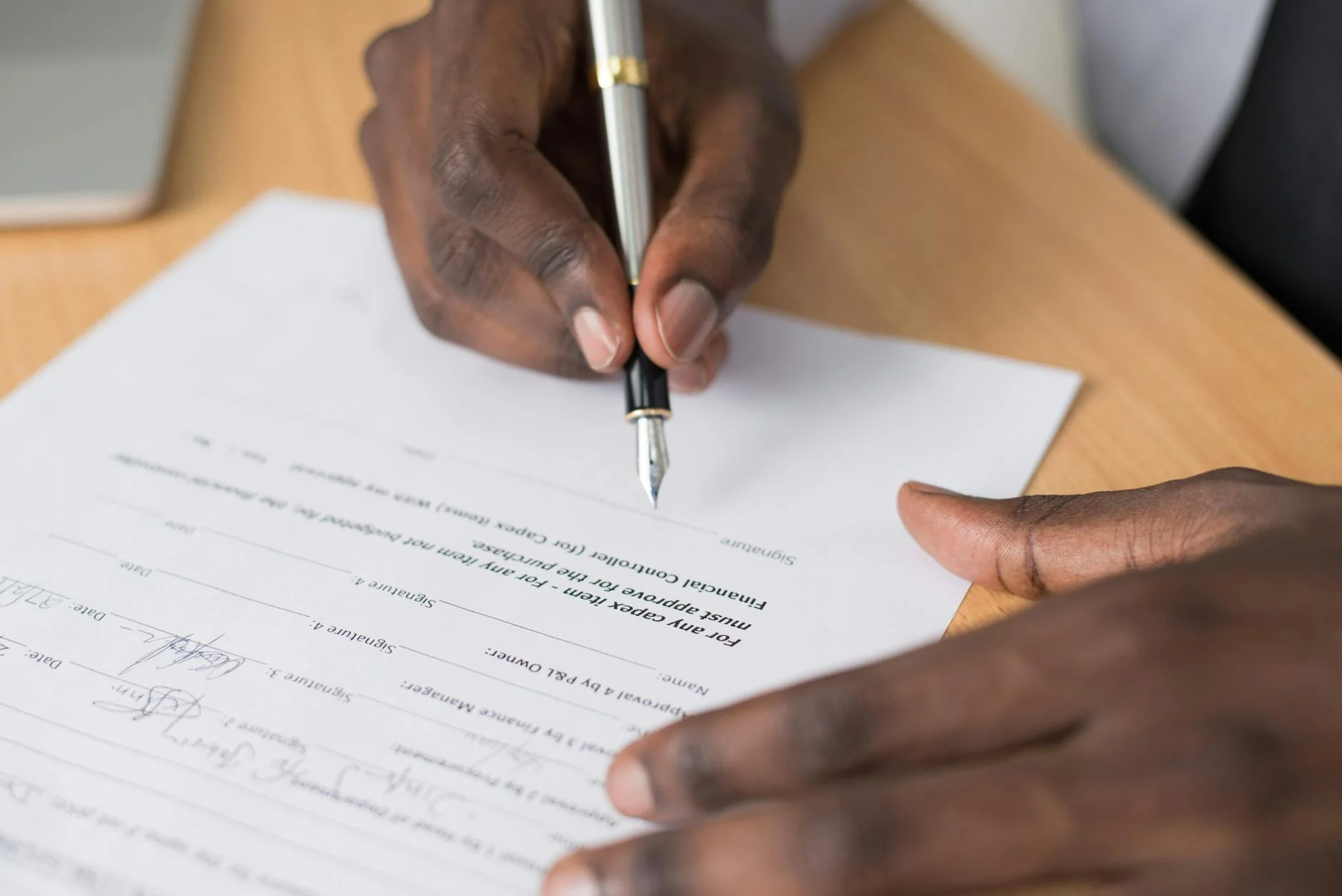 A signed paper document on a wooden desk next to a fountain pen and reading glasses