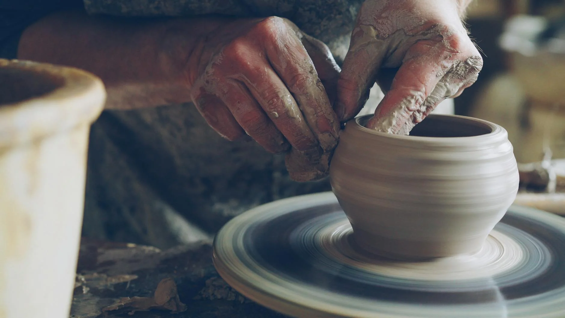 An artisan's hands shaping a clay bowl on a pottery wheel in a small workshop