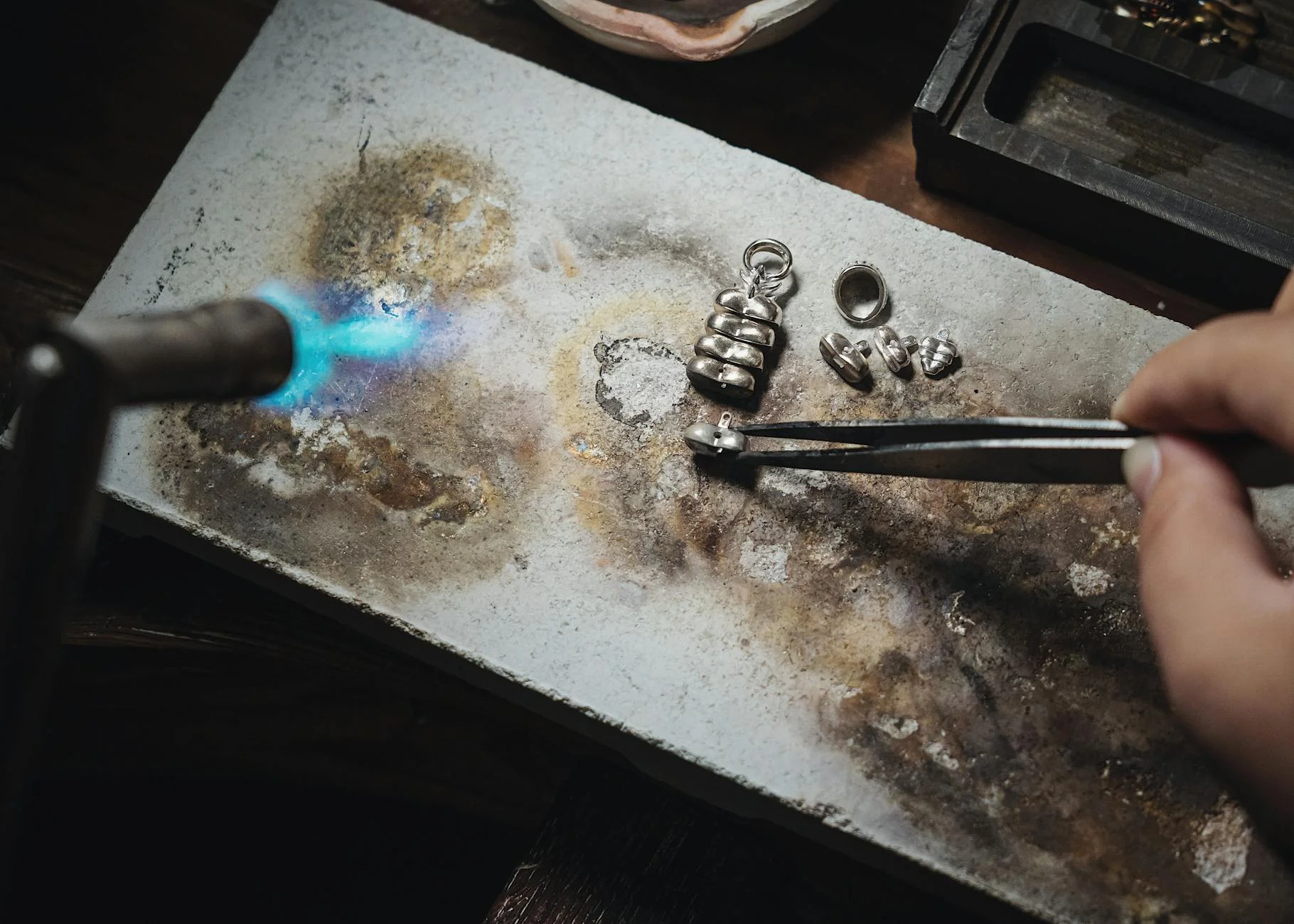 A jeweler's workbench with silver rings, pliers, and a loupe under a bright lamp
