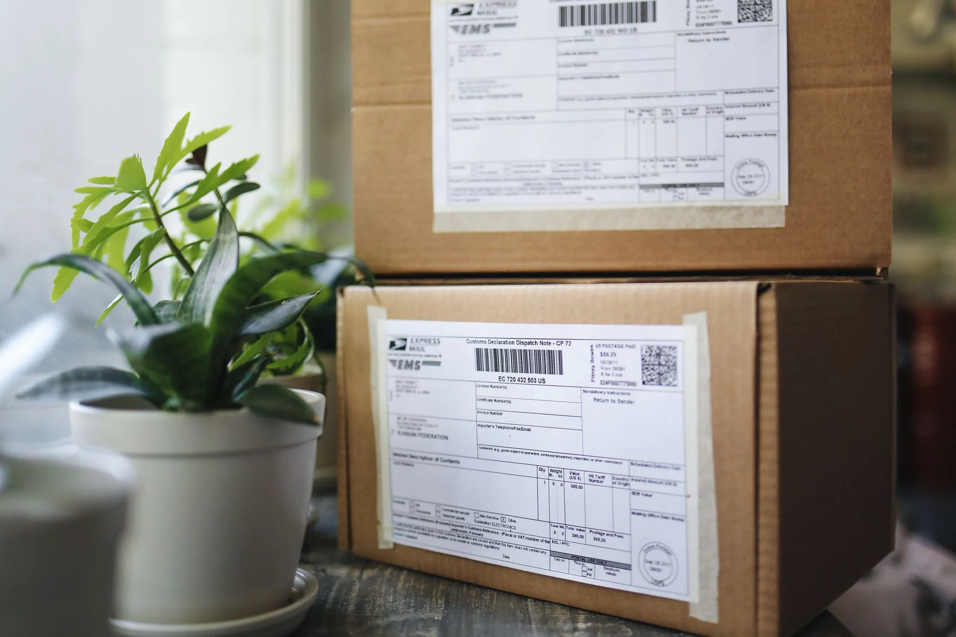 A row of shipping parcels with customs labels on a wooden counter near a window