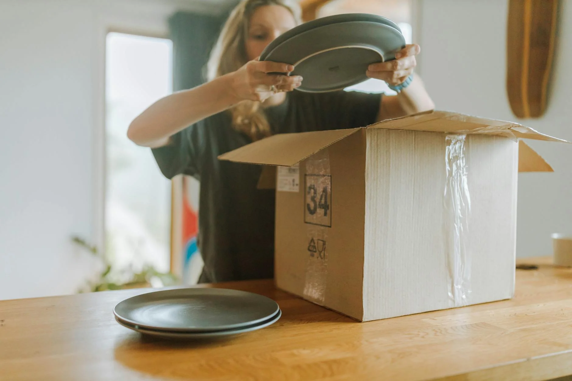 Person packing a single used item into a cardboard box at a kitchen table