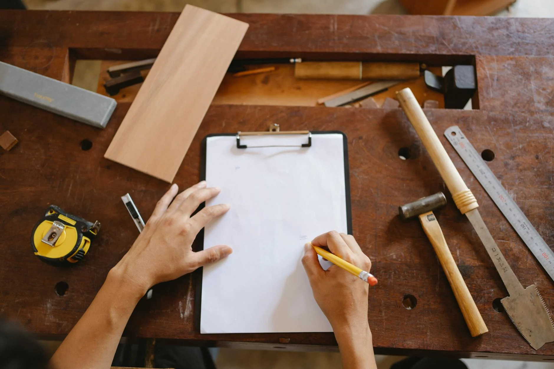 Ein Schreinermeister prüft die abgerundeten Kanten eines Holzstuhls in seiner Werkstatt und macht sich Notizen auf einem Klemmbrett