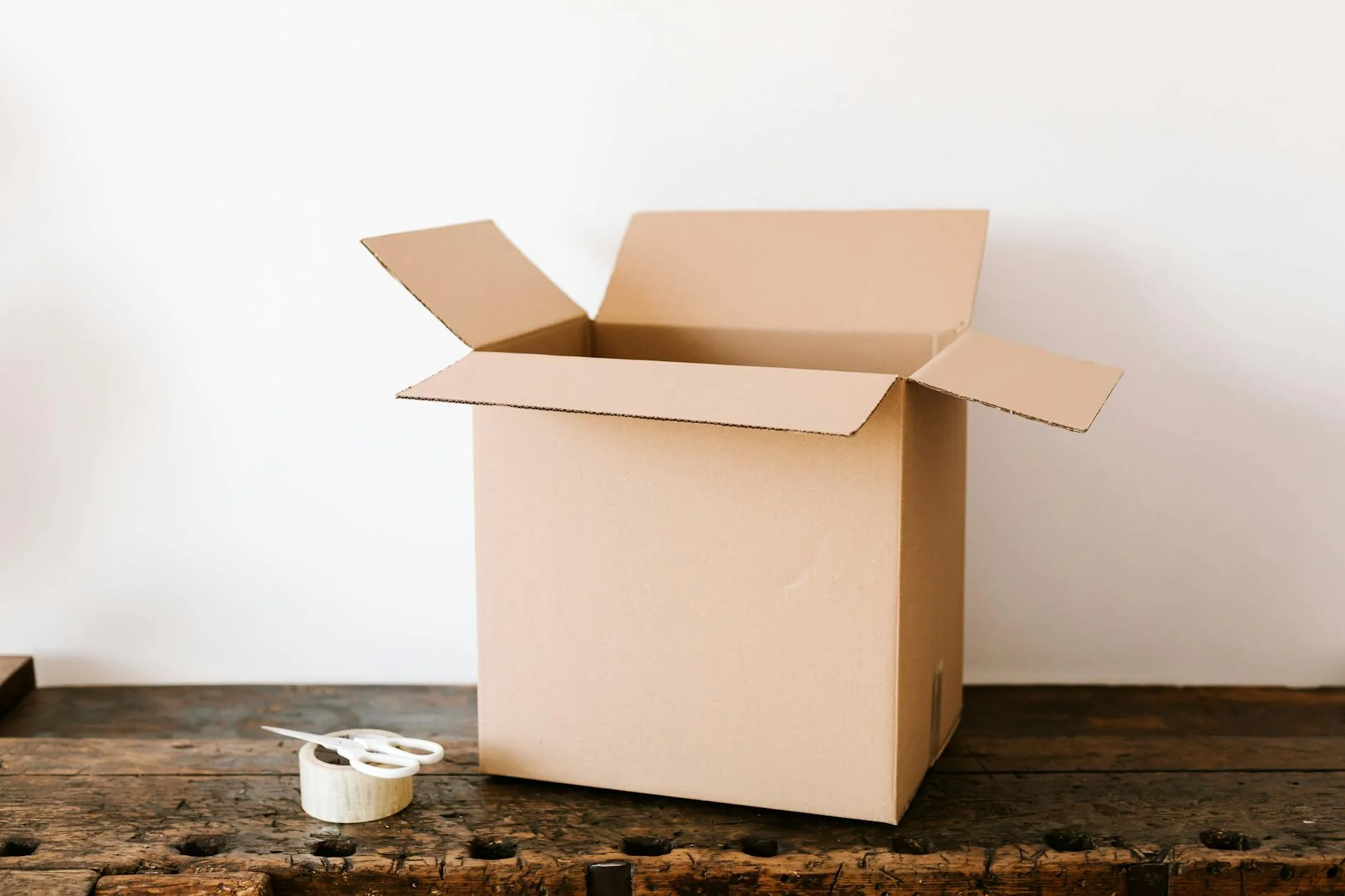 A small business owner packing labeled parcels at a wooden workbench surrounded by shipping boxes