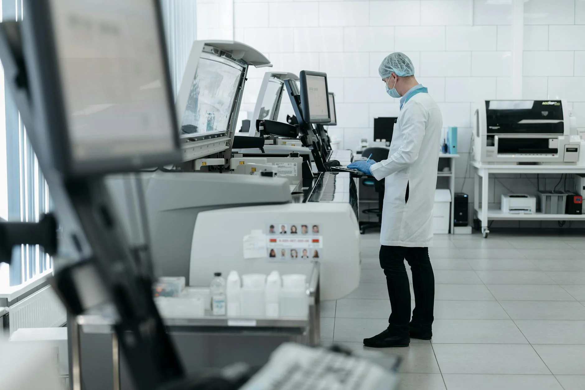 A laboratory technician in a white coat operating testing equipment on a workbench
