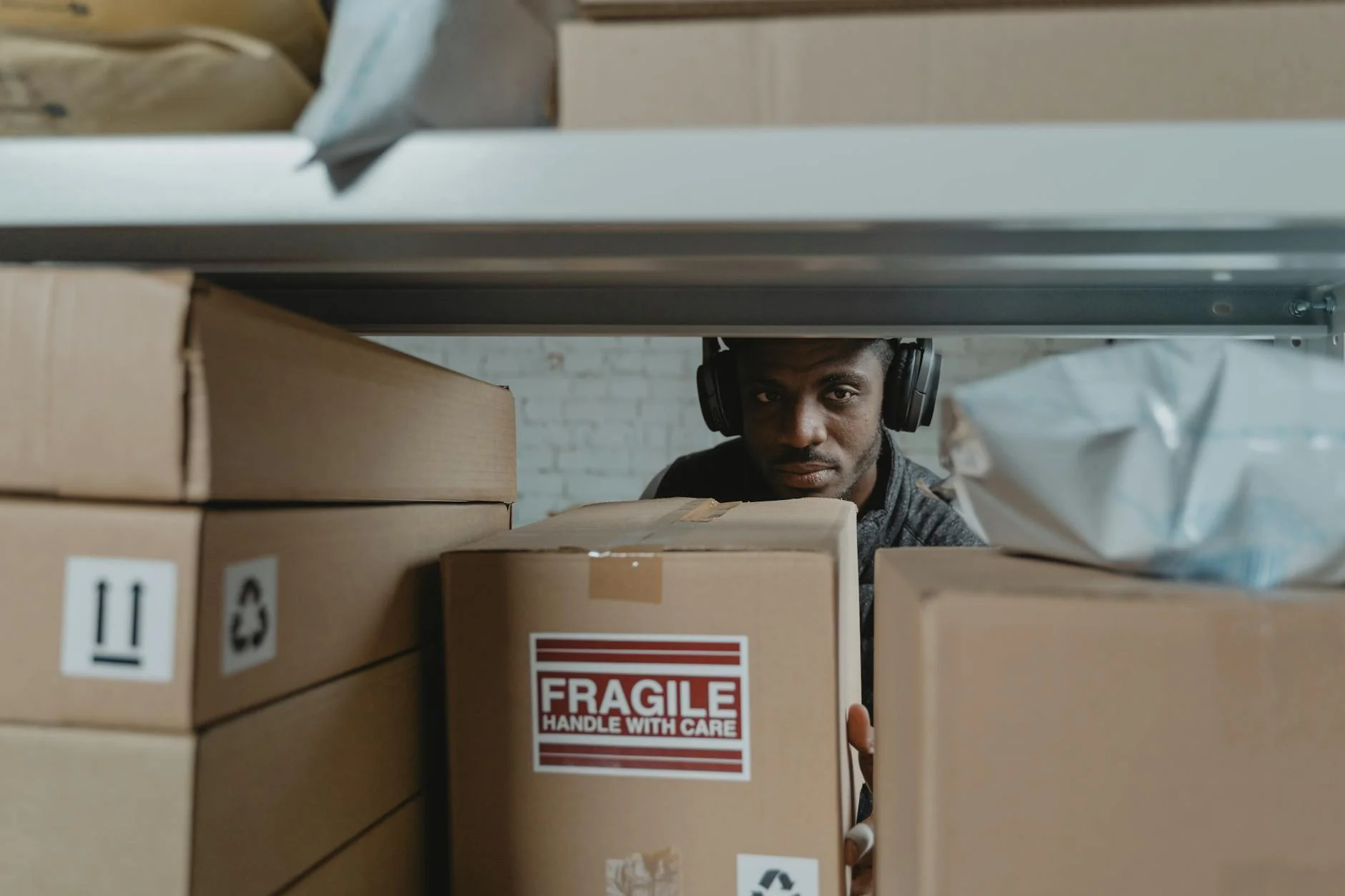A warehouse worker checking the underside of a cardboard product box near a shipping pallet