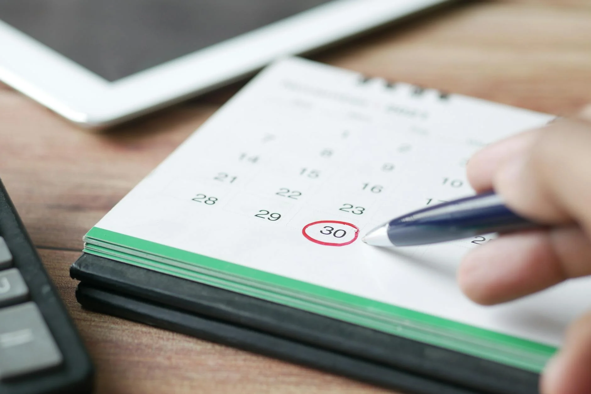 A wall calendar with a date circled in red marker next to a pen